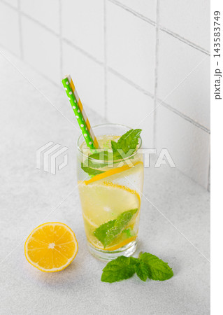 Fresh homemade lemonade with lemon slices, mint and ice in glass on white kitchen tile background Fresh homemade lemonade with lemon slices, mint and ice in glass on white kitchen tile background 143583749