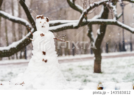 Snowman made of fresh snow standing in winter park during snowfall, surrounded by snow covered trees 143583812
