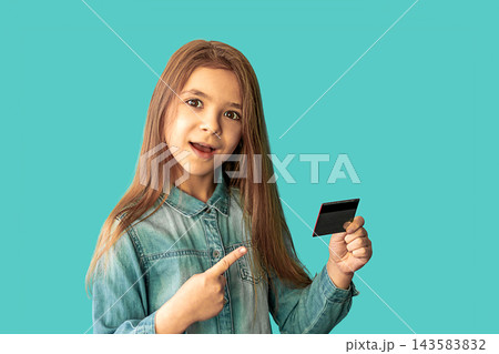 Young girl holding and pointing to a credit card with excited expression on turquoise background 143583832