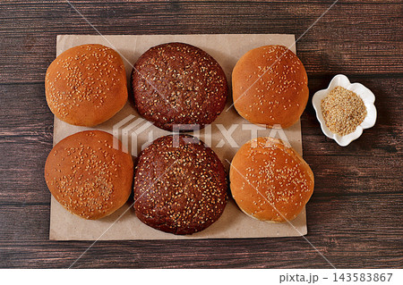 Fluffy buns for burgers, cheeseburgers, and sandwiches. Freshly baked, golden brown sesame seed buns on craft paper atop a kitchen counter,advertisement for cafe or bakery or fastfood restaurant menu. 143583867
