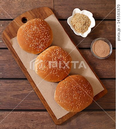 Golden brown, freshly baked sesame seed buns on artisanal food grade on a wooden tray a kitchen counter, fluffy buns for burgers, cheeseburgers and sandwiches. Advertisement for a cafe or bakery, 143583870