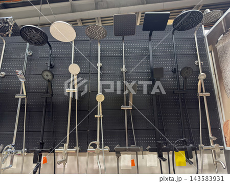 Shower systems line showroom display, with varied overhead rain heads and handheld sprayers mounted against dark perforated panels. Fixtures present finishes and designs for home bathroom renovation. Shower systems line showroom display, with varied overhead rain heads and handheld sprayers mounted against dark perforated panels. Fixtures present finishes and designs for home bathroom renovation. 143583931