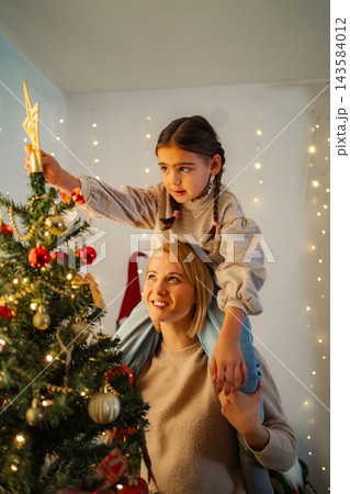 Mother daughter decorating Christmas tree with star topper 143584012