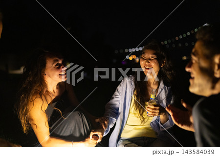 Group shares laughter at night near a bridge with city lights in the background during a social gathering 143584039