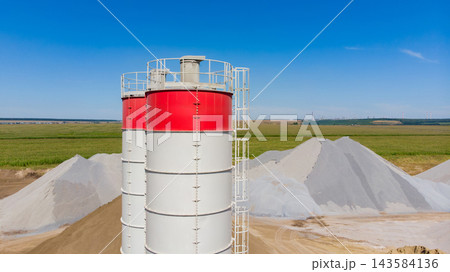 Cement silos and sand piles at a construction site in a rural area under a clear blue sky 143584136