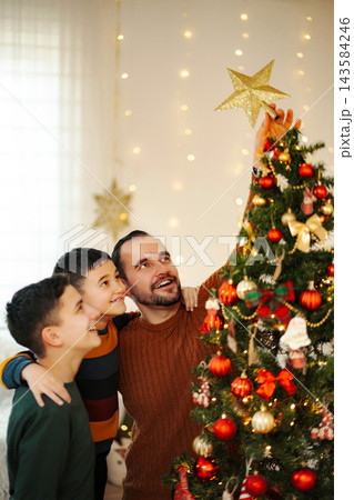 Father and sons placing star on Christmas tree 143584246