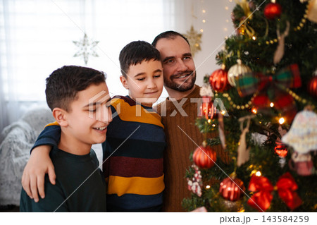 Father and sons admiring decorated Christmas tree at home 143584259