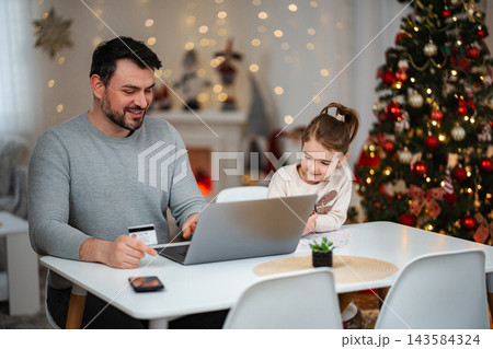 Father and daughter enjoying online Christmas shopping with laptop Father and daughter enjoying online Christmas shopping with laptop 143584324