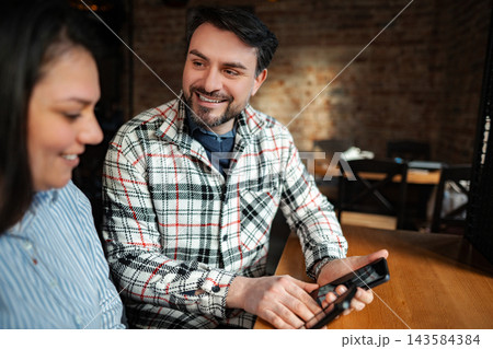 Happy couple sharing content on smartphone in cafe Happy couple sharing content on smartphone in cafe 143584384