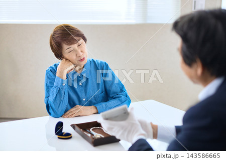 貴金属を査定する買取専門業者とシニア女性 143586665