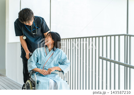 車椅子に乗る女性患者を笑顔で介助する男性医師。病院での患者サポート 143587210