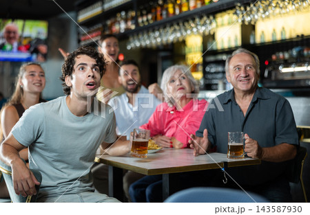 Group of happy friends hangs out at sports bar, watching teams match, and following progress of game. Video broadcast of match or race is available Group of happy friends hangs out at sports bar, watching teams match, and following progress of game. Video broadcast of match or race is available 143587930