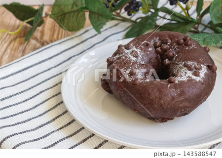 白いお皿に載ったチョコレートがけのベーグル、カフェ風のテーブルコーディネート 白いお皿に載ったチョコレートがけのベーグル、カフェ風のテーブルコーディネート 143588547