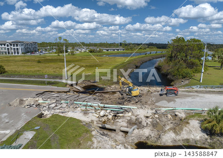 Repair of destroyed bridge after hurricane flood in Florida. Reconstruction of damaged road after flooding water washed away asphalt. Construction equipment at roadwork site Repair of destroyed bridge after hurricane flood in Florida. Reconstruction of damaged road after flooding water washed away asphalt. Construction equipment at roadwork site 143588847