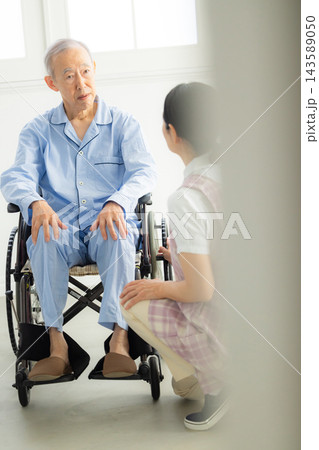 車椅子に乗る男性と介護する女性　 143589050