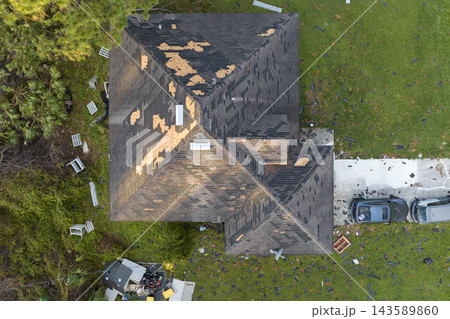 Wind damaged house roof with missing asphalt shingles after hurricane Ian in Florida. Repair of home rooftop concept 143589860