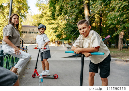 Kids riding scooters in a park with an adult nearby during daytime 143590556