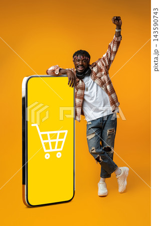 Man enjoys online shopping in front of large mobile screen displaying shopping cart symbol Man enjoys online shopping in front of large mobile screen displaying shopping cart symbol 143590743