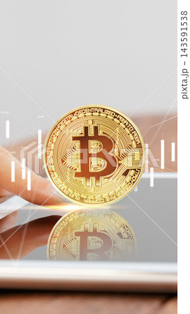 Bitcoin coin held above a tablet with stock market data in the background Bitcoin coin held above a tablet with stock market data in the background 143591538