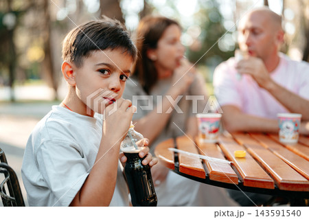 Child drinks soda at a table with family in a park during the afternoon Child drinks soda at a table with family in a park during the afternoon 143591540