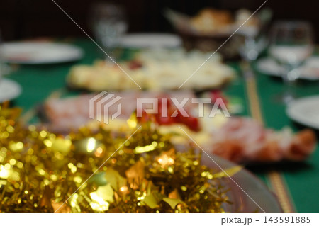 Christmas Eve dinner table showcasing a gourmet spread with ham and cheese platters, gold tinsel decorations, and blurred festive holiday food for a family celebration party Christmas Eve dinner table showcasing a gourmet spread with ham and cheese platters, gold tinsel decorations, and blurred festive holiday food for a family celebration party 143591885