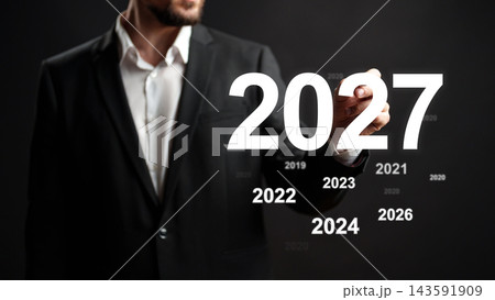Man writing the year 2027 on a blackboard while looking at previous years from 2019 to 2026 in a business setting 143591909