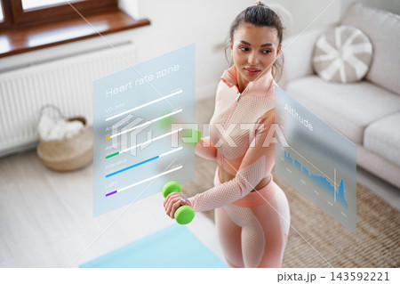 Woman exercises indoors while tracking heart rate and altitude with smart technology Woman exercises indoors while tracking heart rate and altitude with smart technology 143592221