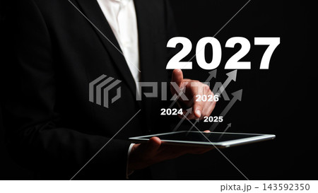 Growth trends presented through a hand pointing at a tablet with the year 2027 highlighted Growth trends presented through a hand pointing at a tablet with the year 2027 highlighted 143592350