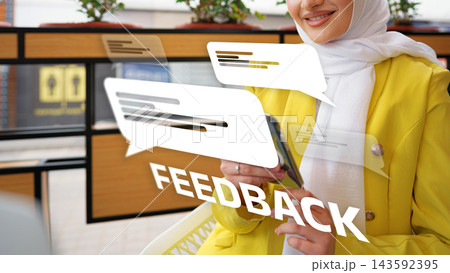 Woman in a yellow jacket sitting in cafe while using her phone and engaging with feedback Woman in a yellow jacket sitting in cafe while using her phone and engaging with feedback 143592395