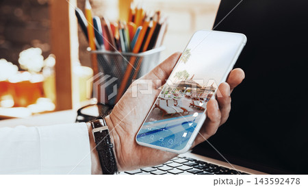 Person using smartphone for social media chats and calls while sitting at a desk with a computer and stationery in view Person using smartphone for social media chats and calls while sitting at a desk with a computer and stationery in view 143592478