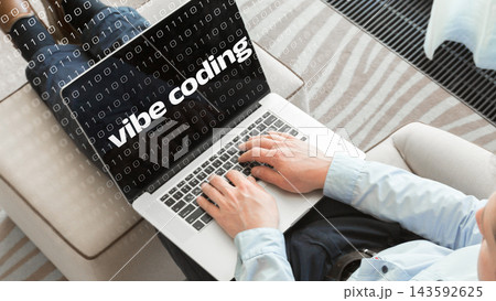 Person coding on laptop with words vibe coding displayed on screen in a cozy indoor space 143592625