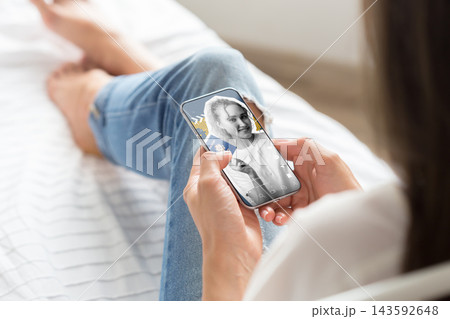 Person using smartphone for social media chats and calls while sitting on a bed during daytime 143592648