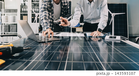Two Asian engineers wearing hardhats and safety vests discussing solar panel installation and renewable energy project in the office. Two Asian engineers wearing hardhats and safety vests discussing solar panel installation and renewable energy project in the office. 143593107