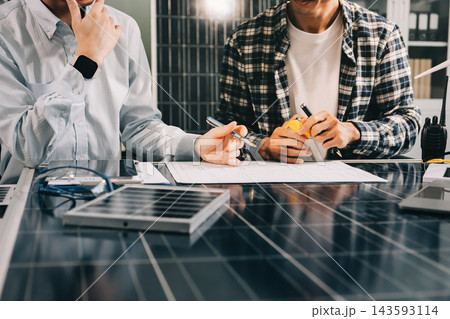 Two Asian engineers wearing hardhats and safety vests discussing solar panel installation and renewable energy project in the office. Two Asian engineers wearing hardhats and safety vests discussing solar panel installation and renewable energy project in the office. 143593114