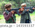 Two men in berets aiming AK-47 rifles in forested outdoor setting with focused expressions 143593337