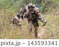 Soldier carrying injured comrade through tall grassy terrain with focused determination 143593341