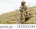 Soldier in full tactical gear leans on metal railing overlooking hilly jungle terrain with focused gaze 143593344