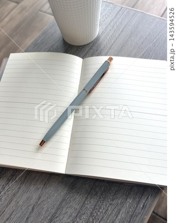 木目調デスクに置かれた開いたノートとペンとコーヒーカップ（縦構図・コピースペース）⁠ 143594526