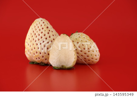 Unique white pineberry strawberries, one sliced in half, displayed on a vibrant red background Unique white pineberry strawberries, one sliced in half, displayed on a vibrant red background 143595349