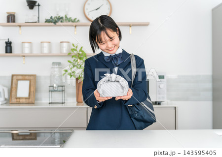 家のキッチンでお弁当を持って笑顔を見せる制服姿の女子高校生 家のキッチンでお弁当を持って笑顔を見せる制服姿の女子高校生 143595405
