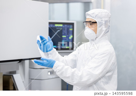 半導体製造工場のクリーンルームで防護服を着用しシリコンウエハーを確認する作業員 143595598