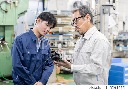 製造工場で外国人労働者に機械部品や製品について説明する日本人社員・外国人材への技術指導と人材育成 製造工場で外国人労働者に機械部品や製品について説明する日本人社員・外国人材への技術指導と人材育成 143595655