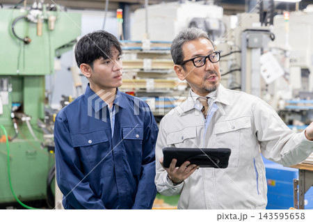 製造工場で外国人労働者にタブレット端末を使って作業内容や業務について説明する日本人社員・外国人材への 143595658