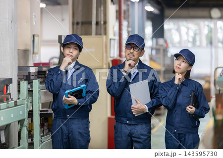 製造工場で設備を見ながら顎に手を当てて考える若手男女作業員とベテラン男性技術者 製造工場で設備を見ながら顎に手を当てて考える若手男女作業員とベテラン男性技術者 143595730
