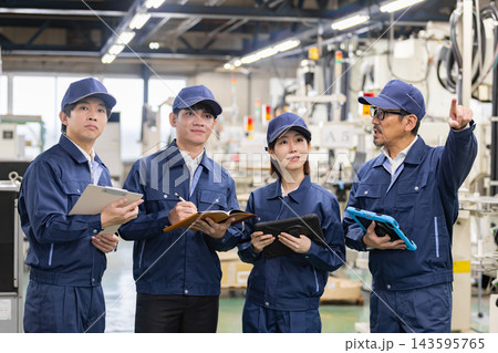 工場内で設備を指差しながら作業指示と説明を行う男性とメモを取る多国籍の製造業スタッフ4人 143595765