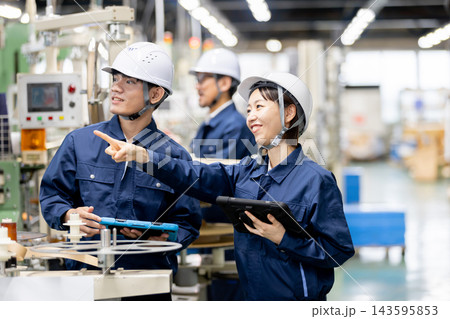 製造工場で外国人男性作業員と日本人女性作業員がタブレットを使いながら生産設備について打ち合わせをする 143595853