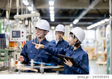 製造工場で外国人男性作業員と日本人女性作業員がタブレットを使いながら生産設備について打ち合わせをする 製造工場で外国人男性作業員と日本人女性作業員がタブレットを使いながら生産設備について打ち合わせをする 143595855