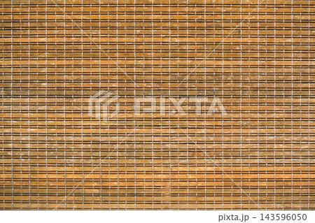 Close-up of a natural bamboo mat or blind, featuring horizontal light brown wooden slats intricately woven together with contrasting white threads. A rustic and textured background. Close-up of a natural bamboo mat or blind, featuring horizontal light brown wooden slats intricately woven together with contrasting white threads. A rustic and textured background. 143596050