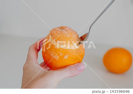Hand holds a frozen orange filled with homemade sorbet while a spoon scoops the creamy dessert from the fruit peel. Serving idea for dairy free dessert recipes and summer menus. 143596696