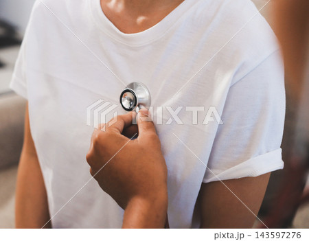 A young male doctor uses a stethoscope to examine a young female patient seated on a couch indoors. A young male doctor uses a stethoscope to examine a young female patient seated on a couch indoors. 143597276